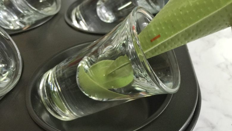 抹茶巧克力双色酸奶杯, 杯子放在马芬模具里斜放,用裱花袋把抹茶酸奶挤入杯底。