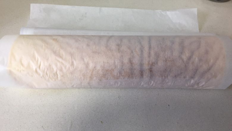 虎皮蛋糕卷,擀面杖卷起油纸,起头轻压一下顺势卷起蛋糕卷,放置一边静置定型。