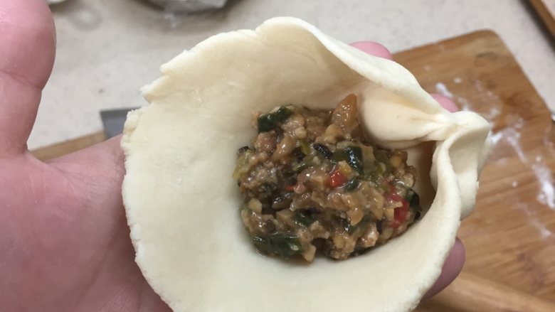 香菇肉馅包,一个大拇指按住皮不动,食指和中指捏小褶子往大拇指收拢