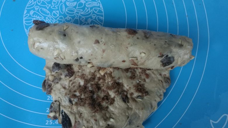 无油健康版 黑糖干果软欧,将有果料的面团擀成椭圆形,撒上一层红糖,自上而下卷起,捏紧。