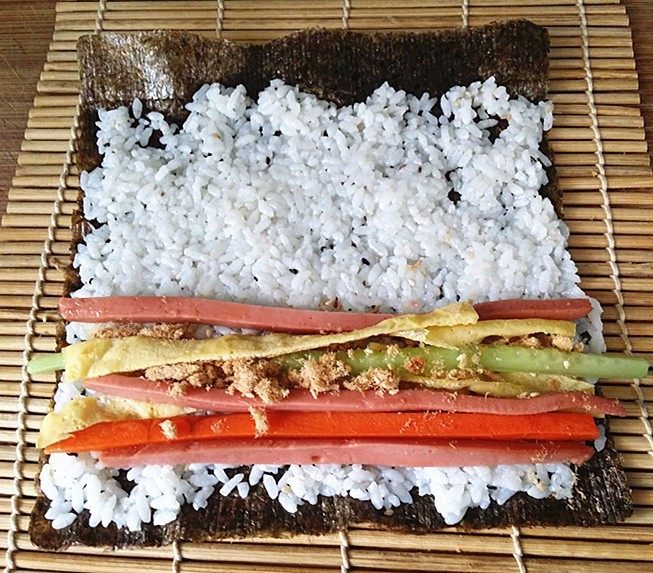 什锦火腿寿司,将饭团往四周推平,在下端摆放蛋皮、黄瓜、火腿、肉松和胡萝卜