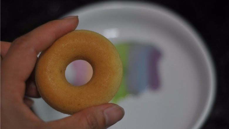 蔬菜汁彩虹甜甜圈,把甜甜圈盖在排列好的糖霜上,所有颜色 都沾上,稍微用力压一压,让周围都粘上
