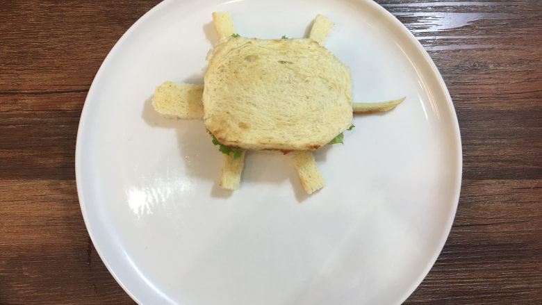 童趣早餐——乌龟全麦三明治,用切剩下的面包边角料切出乌龟的头、脚和尾巴,摆放在乌龟的身体旁边。
