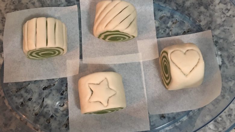 雙色抹茶饅頭,底下墊烘焙紙,用手從切面拿起饅頭,排入蒸籠並略微整型。蓋鍋蓋進行發酵(約45~60分鐘),依室內溫度的不同發酵時間也會有差別。
切下來的頭尾可以合起來輕壓,就又變另一顆饅頭了。
如想切割花紋則在發酵前進行。