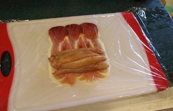 鮟鱇鱼生火腿佐芒果酱汁,铺一张保鲜膜,摆上生火腿片。将鱼肉摆上。