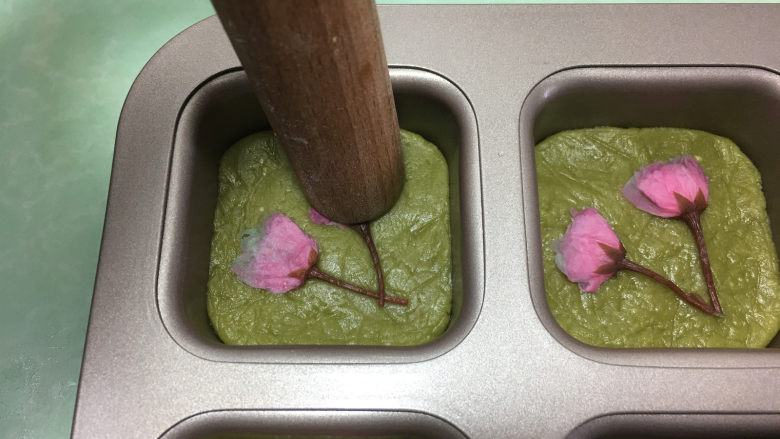 樱花抹茶凤梨酥,将提前浸泡的樱花用厨房用纸擦干水份,整理好形状后摆放在凤梨酥上,然后再用擀面杖顶端压平。