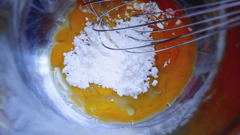 芒果千层蛋糕,把鸡蛋敲在容器里,加入糖粉,用手动打蛋器搅拌均匀。