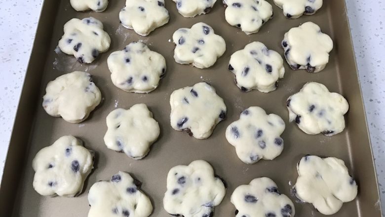 蜜豆炼乳司康饼,取出放入不粘烤盘,剩余的面团继续揉成团,再擀平,按出花型,重复到面团用完。此时预热烤箱,上下火200度。