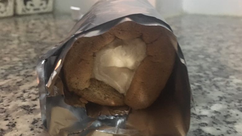 摩卡咖啡戚风蛋糕卷,抬起靠近自己这边的铝薄纸,让蛋糕边对边的卷起,并将两边转紧即可入冰箱冷藏30分钟。