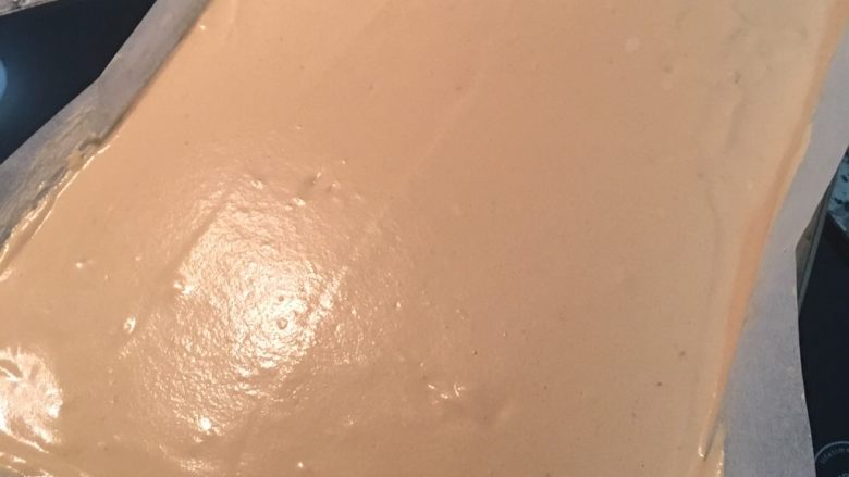摩卡咖啡戚风蛋糕卷,倒入铺有烘焙纸的烤盘中,轻轻铺平后,记得要把烤盘提起摔下让空气跑出来,接着放入烤箱烤8分钟后,取出烤盘转头,再入烤箱烤9-10分钟;