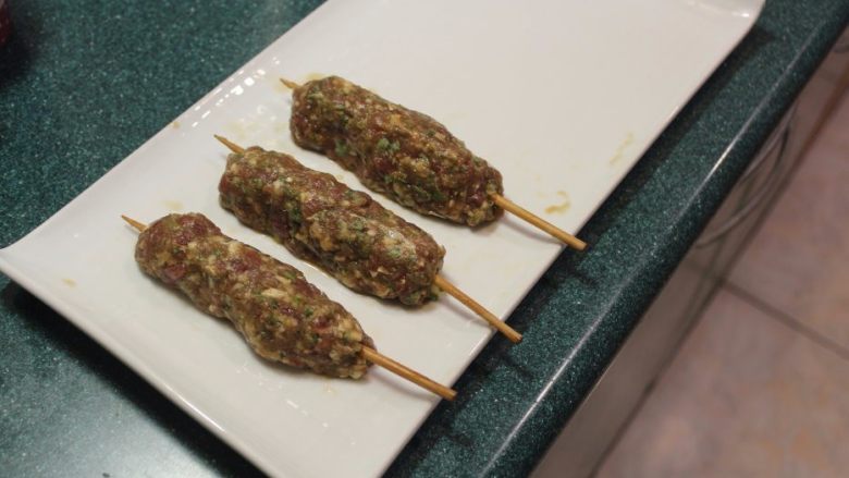 串烧羊肉卷(巴基斯坦风),拿一根竹签,将适量的羊肉泥塑型成长型肉串在竹签上。