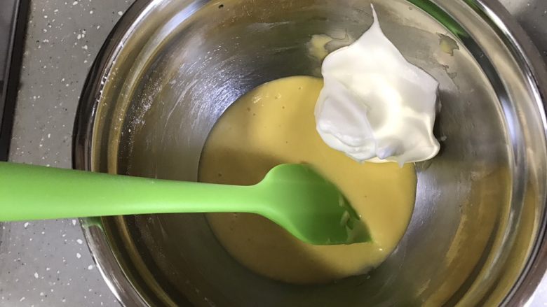 巧克力可可蛋糕卷,将小部分蛋白霜加入蛋黄糊,用翻拌的手法翻拌均匀。
