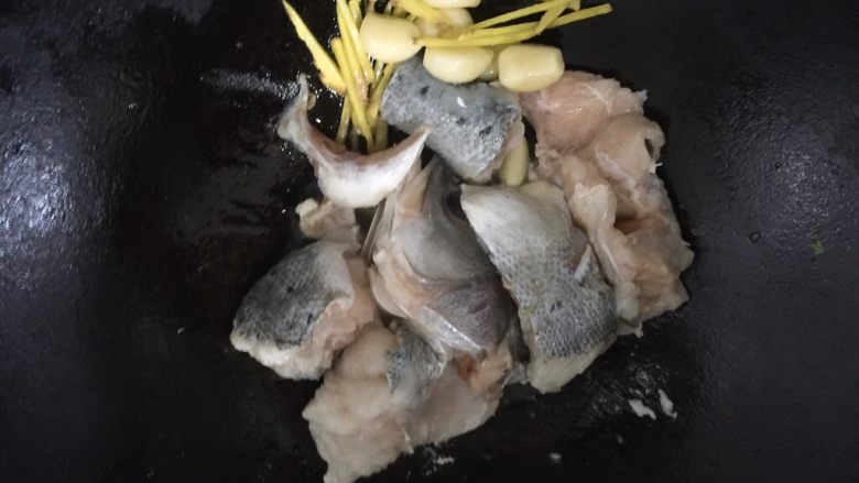 酱烧海鲈鱼,把姜丝和蒜瓣撇一边去,依旧中火,放鱼段下锅煎制。几分钟后翻下面,锅内油多的话外皮呈金黄色时即可。