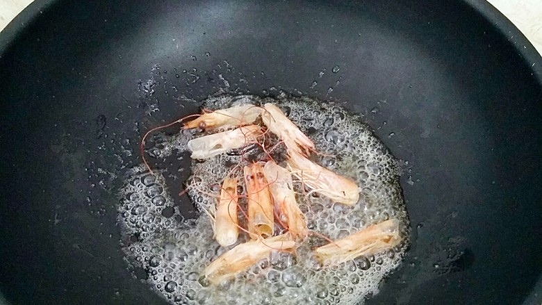 鲜虾菌菇面,锅中放油,烧热放入虾头炒出虾油,捡出虾头。