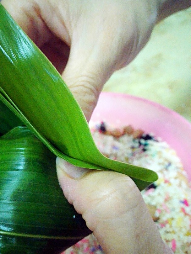 彩米花生香菇肉粽,包法主要在这步,左手手指往里压挤,右手也粽叶折上。