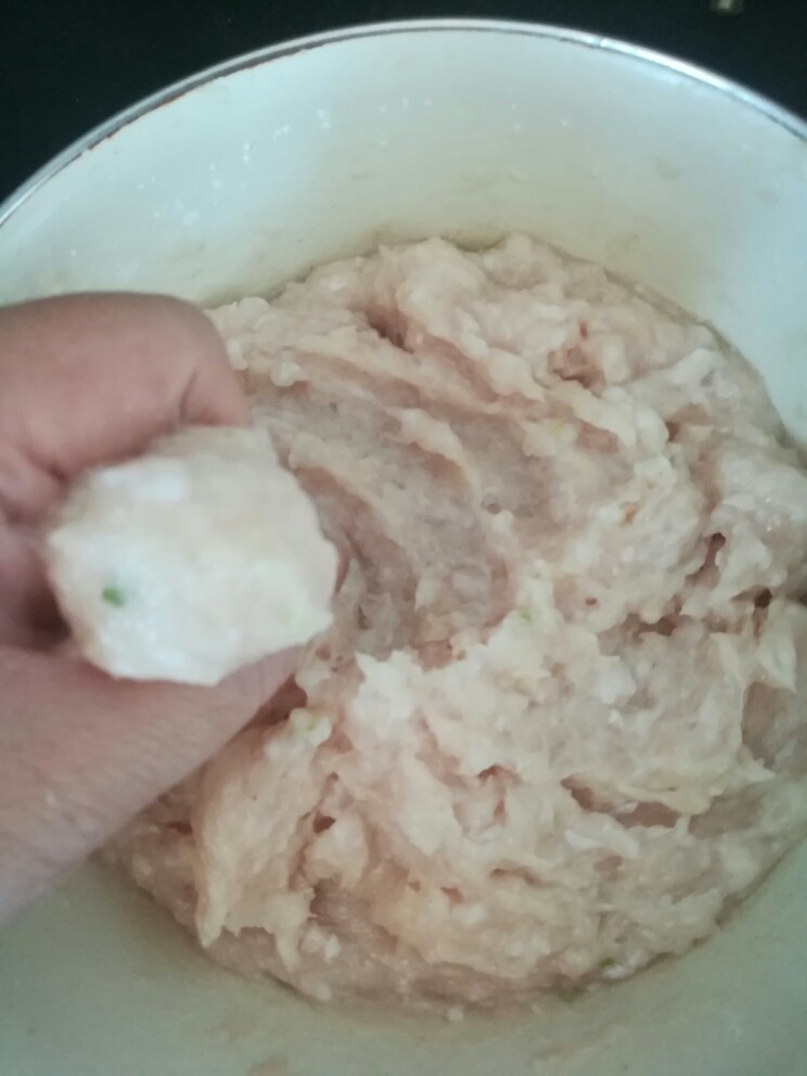 鱼丸干贝汤,左手抓一把鱼肉泥,先用大拇指扒一下(使丸子表面光滑),挤出来,右手拿小匙刮下来放入水中。(也可以不拿小匙,用右手食指刮下来,丸子会更圆滑漂亮)