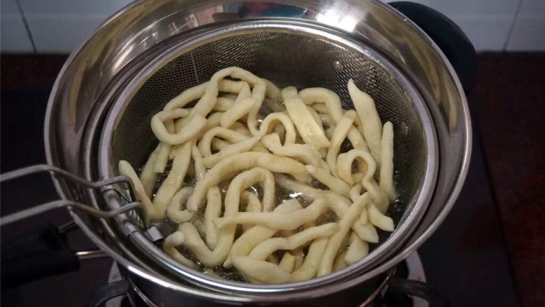 蔓越莓沙琪玛,将一条坯条放入油锅试油温,若坯条迅速浮起涨大表示油温可以,开始放入坯条,炸坯条
