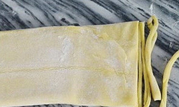 蔓越莓沙琪玛,在面团上撒上玉米淀粉防粘,然后擀成0.2厘米厚的薄片。用披萨轮刀切成细坯条,在皮条上撒上玉米淀粉防粘