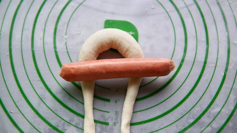 香肠兔子馒头,把搓长的面团摆成如图的锁形,也是一个倒"U"型,把<a style='color:red;display:inline-block;' href='/shicai/ 425'>香肠</a>放在面团上,如图所示