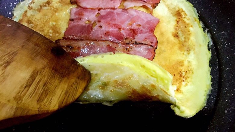 手抓饼版培根鸡蛋饼,将培根片夹起,放入煎好的手抓饼,鸡蛋一面向上,将培根片并排摆放在当中
用筷子和铲子配合卷起