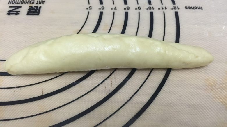 心形玉米火腿沙拉包,由上至下卷起,收紧收口,呈橄榄长形的面团。用刀横着切开面团,呈V字型