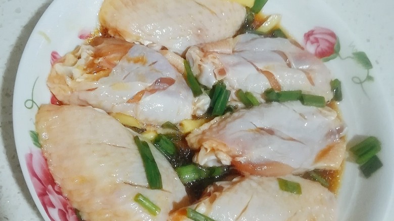 可乐鸡翅,鸡中翅洗干净,用刀在两面切割,方便调味料渗入鸡肉,加入葱花,一小片切姜,少量酱油、耗油、料酒腌制半个钟。