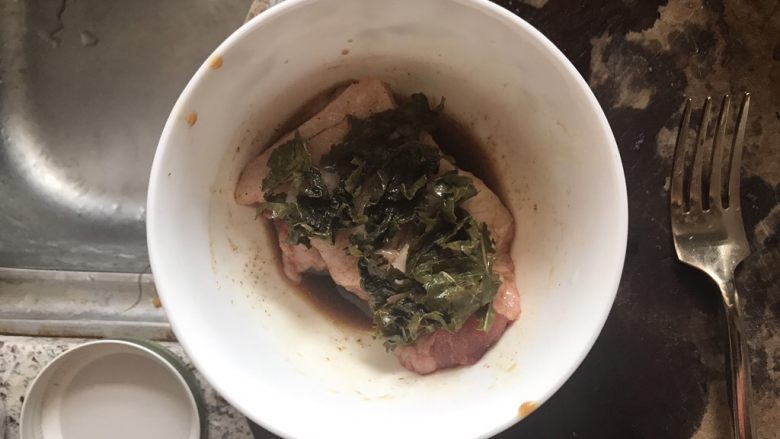 茶香猪颈肉,猪颈肉放入碗中,抓匀调料,铺上一层绿茶叶,腌制一晚