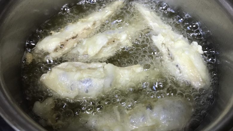 油炸穿条鱼,捞出第一条炸好的小鱼后,再多次放入大小相近的鱼,进行油炸