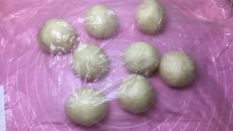 火腿肠辫子面包,将发酵好的面包取出进行排气的,然后平均分割成8份,滚圆后盖保鲜膜醒发10分钟。