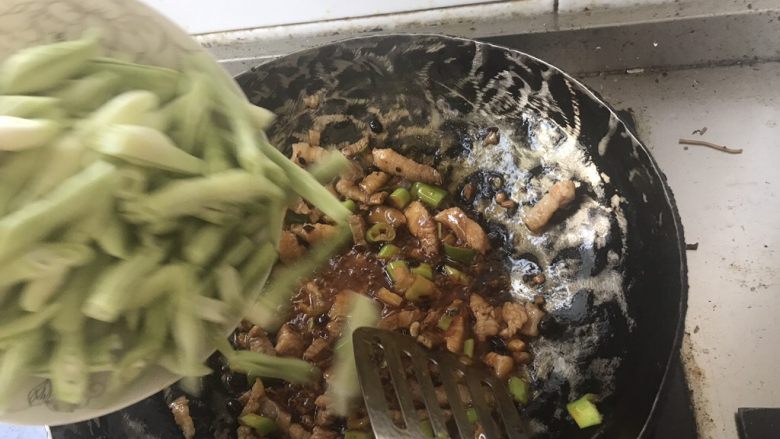 豆角焖面,锅里倒油预热并加入<a style='color:red;display:inline-block;' href='/shicai/ 10084'>老干妈</a>三勺一起预热，油七八成熟的时候放入葱姜末，待爆出葱姜香味的时候，放入味达美酱油、五花肉块，反复翻炒。五花肉变色之后，开始放豆角条。翻炒五分钟。