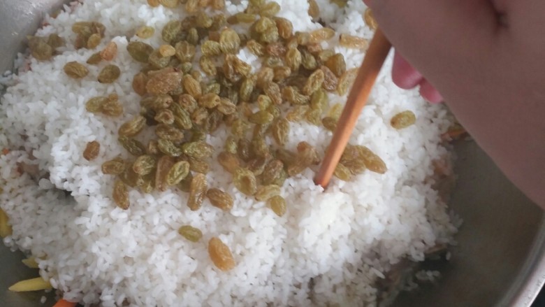新疆羊排抓饭,倒入米讲葡萄干撒到上面,用筷子到几个洞,然后盖上锅盖焖十五分钟。
