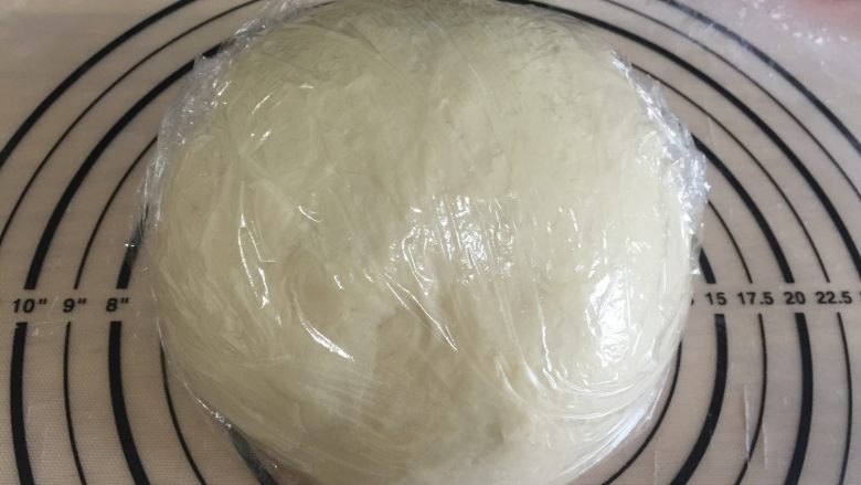 炼奶提子吐司,揉面好之后的面团放在案板上,包上保鲜膜,静置松弛20分钟