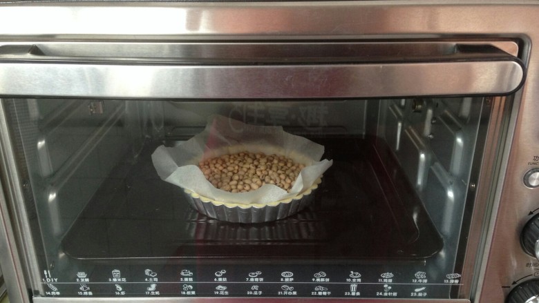 法式咸派,用叉子在派皮上插出小孔,然后在派皮上面铺盖一张油纸,放上干黄豆,放进预热到180度的烤箱下层烘烤15分钟,然后取出油纸和黄豆,再烘烤五分钟放凉备用。