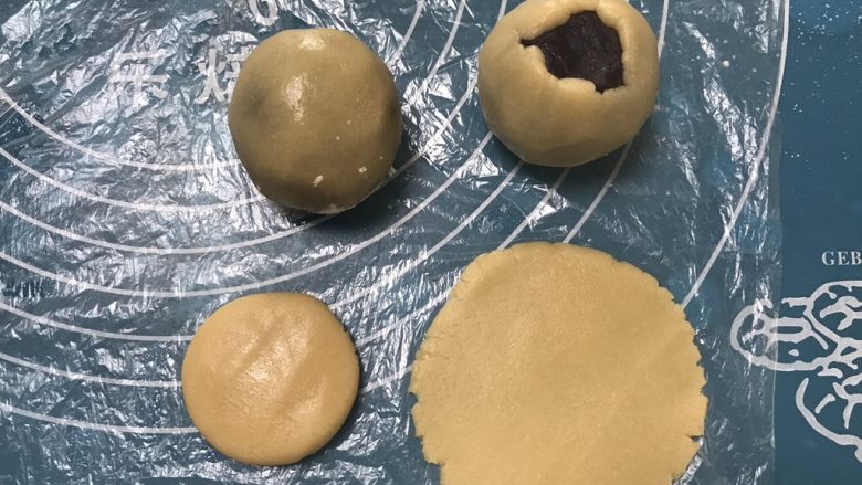 广式红豆沙月饼,取一个面团用手掌摁一下擀成圆形,包上豆沙用虎口慢慢收紧,