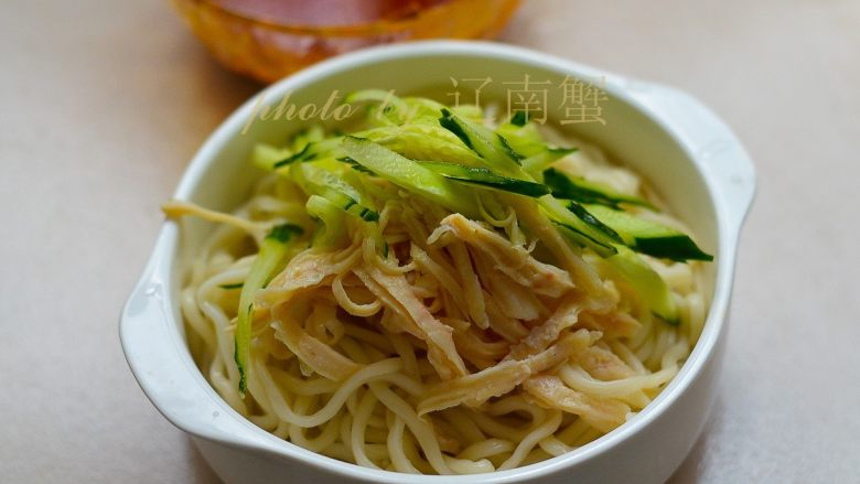 鸡丝凉面,过凉后的面条捞出,沥水装碗,放上肉丝和黄瓜丝。