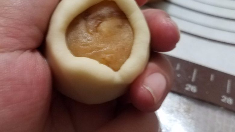 桃山皮月饼,把白色桃山皮搓成球,用刮板压扁,然后轻轻的把皮拿起来,放在手部虎口位置,上面放上搓好的馅料,一点一点慢慢收紧,一定注意要馅料跟皮完全贴紧,否