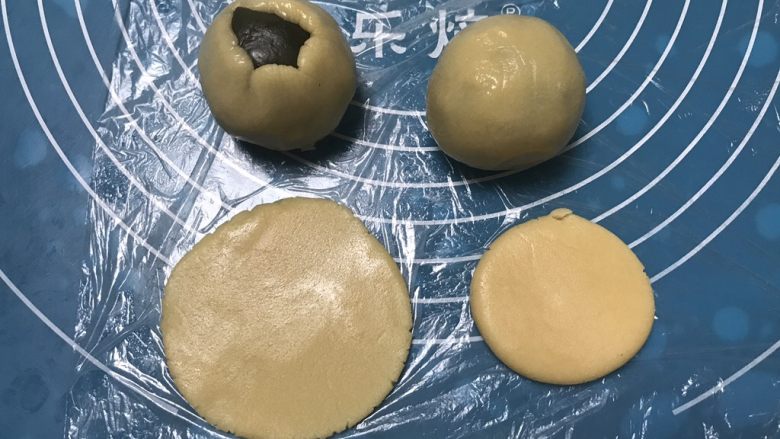 广式抹茶蛋黄月饼,取一个面团用手掌摁一下擀成圆形,包上抹茶馅,用虎口慢慢收口