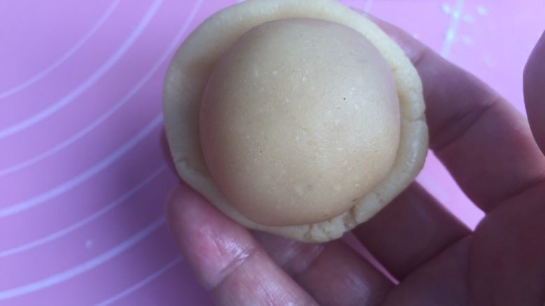 莲蓉蛋黄月饼(50克),手上沾点油防粘。把饼皮捏成弧形底的小圆皮。放入馅料。