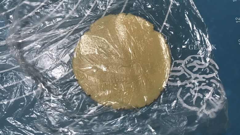 广式五仁月饼,取一个面团放在保鲜膜上用手掌摁一下 ,然后上面盖上保鲜膜擀成圆形,