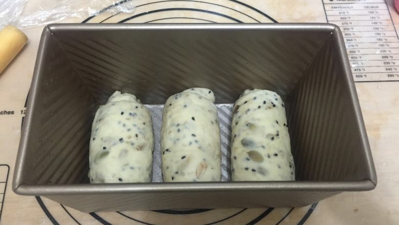 果仁吐司 直接法,吐司盒的塑形是比较复杂一些。首先将面团擀成椭圆形,上下的面饼往中间折之后收紧收口,旋转90度竖着擀开,压薄底边后卷起收口。放入土司盒中
