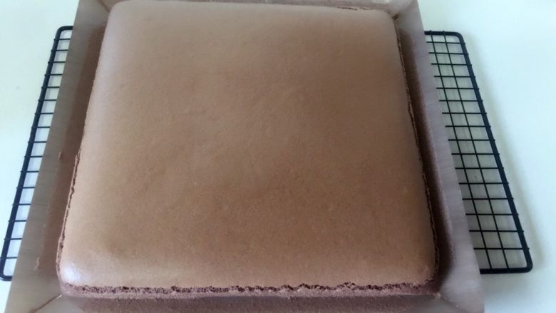 可可奶油瑞士卷,烘烤结束马上拿出烤盘,把烤盘往台面上摔一下,震出内部的大气泡,连同油布移至晾网架上散热。