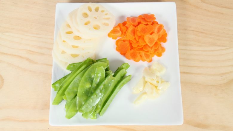 农家小炒,将莲藕去皮切片,荷兰豆去两端蒂头、撕去筋络,胡萝卜去皮,用模具摁出心形跟梅花图案,大蒜拍碎,取出外壳。