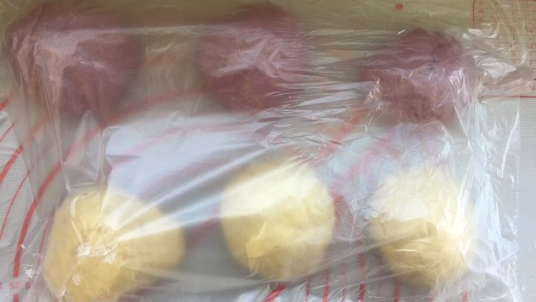 面包机版 紫薯双色吐司,将原味,紫薯面团均匀的各分三份,滚圆后,包上保鲜膜发酵20分钟。