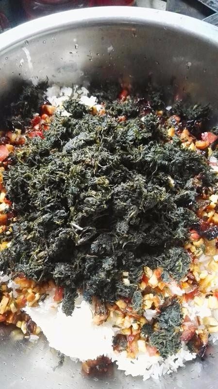 侗家社饭的做法,把炒好的花生、豆腐干、腊肉腊肠放入,再放入蒿菜、大蒜、野葱,搅拌均匀。