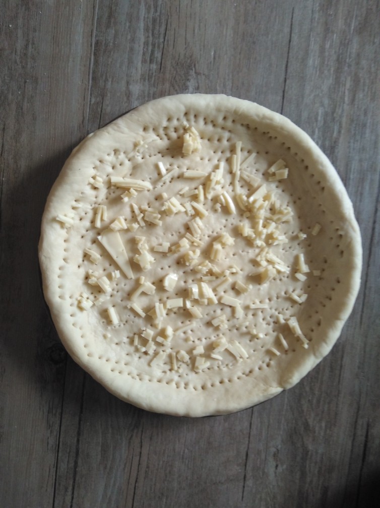 爽口菠萝火腿披萨,面团发好了就擀成面皮做出披萨的底。

我没有擀面杖也没有披萨盘，面皮是用手摊的，披萨盘我是用家里普通的陶瓷盘，也可以直接摊好形状放到烤盘里。

摊好了拿叉子在盘底扎点小孔防止受热膨胀。

扎好了铺上一层马苏里拉芝士。