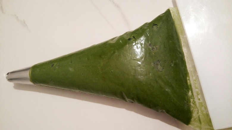 云朵抹茶曲奇,用的是8齿的裱花钉,裱花丁装入裱花袋,裱花袋前面剪一个小口,再把裱花袋套入一个杯子,装入面糊,装好以后,放在台板上,刮板把上面的全部刮下去