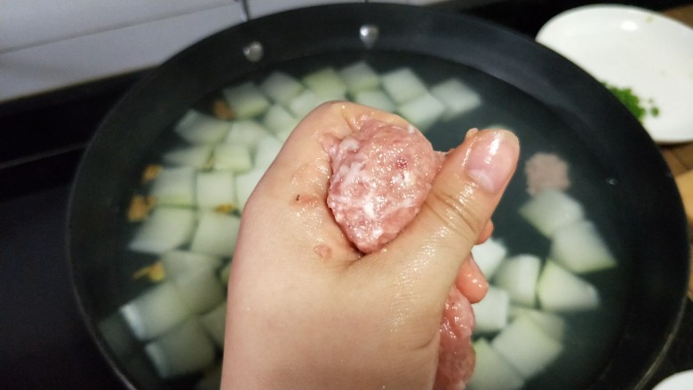 冬瓜圆子汤,冬瓜煮八成熟时转小火,手抓一把肉馅,用虎口挤出一小肉团,勺子沾下水,将肉丸刮到锅里