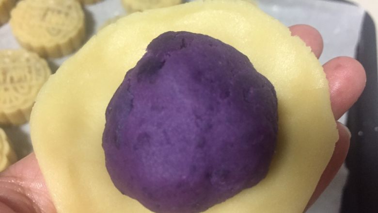 广式月饼(紫薯蛋黄馅),醒好的月饼皮面团称重分成40克一个的小剂子,取一个小剂子捏成圆片紫薯蛋黄放在面皮中间
