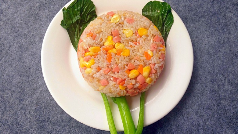 向日葵蛋包饭,取一个盘子,把焯好水的青菜铺在底下,米饭放小碗中用勺子压实,倒扣在盘子中间。
