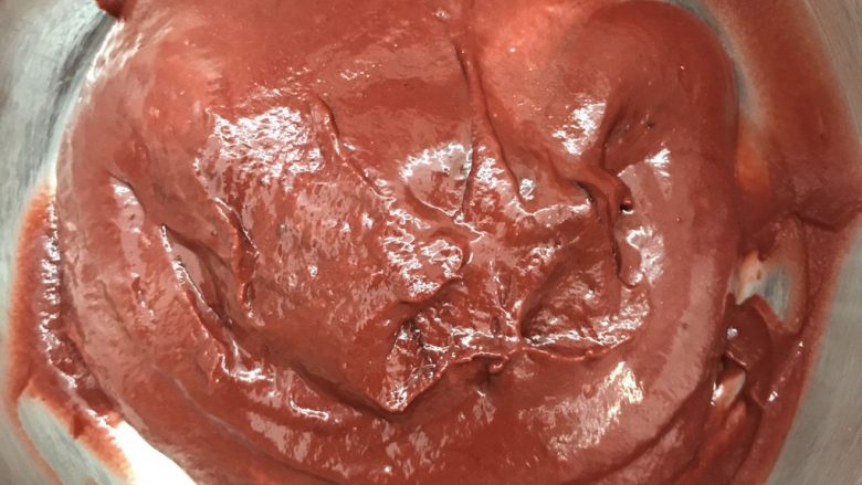 奶酪西瓜蛋糕,制作红丝绒蛋糕坯:色拉油和牛奶混合乳化,加入蛋黄打匀,加入红丝绒液,筛入低粉和可可粉,翻拌均匀。